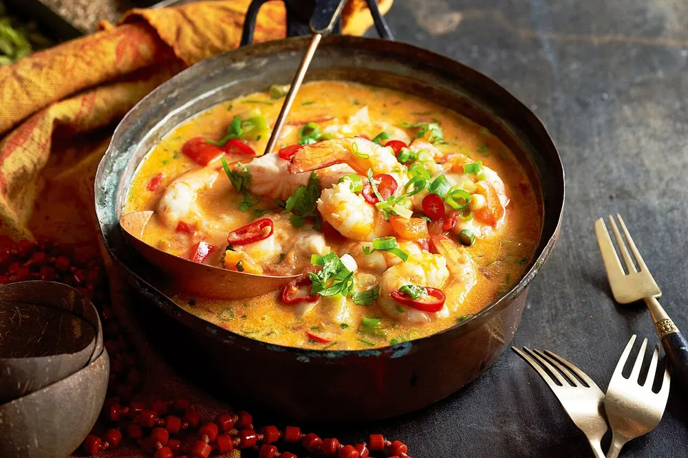 A pot of shrimp moqueca with red chili and scallions in a golden broth